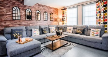 A modern living room with a grey sectional sofa, a wooden coffee table, and a brick wall with arched windows.