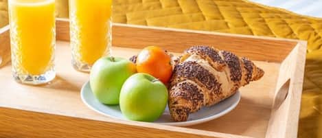 A breakfast tray with croissants, apples, and orange juice on a bed with a yellow quilt and a pillow with "Sleep" written on it.