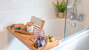 Une salle de bain avec un plateau en bois contenant divers articles de toilette, une douche en verre et une plante en pot.