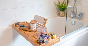 A bathroom with a wooden tray holding various toiletries, a glass shower enclosure, and a potted plant.