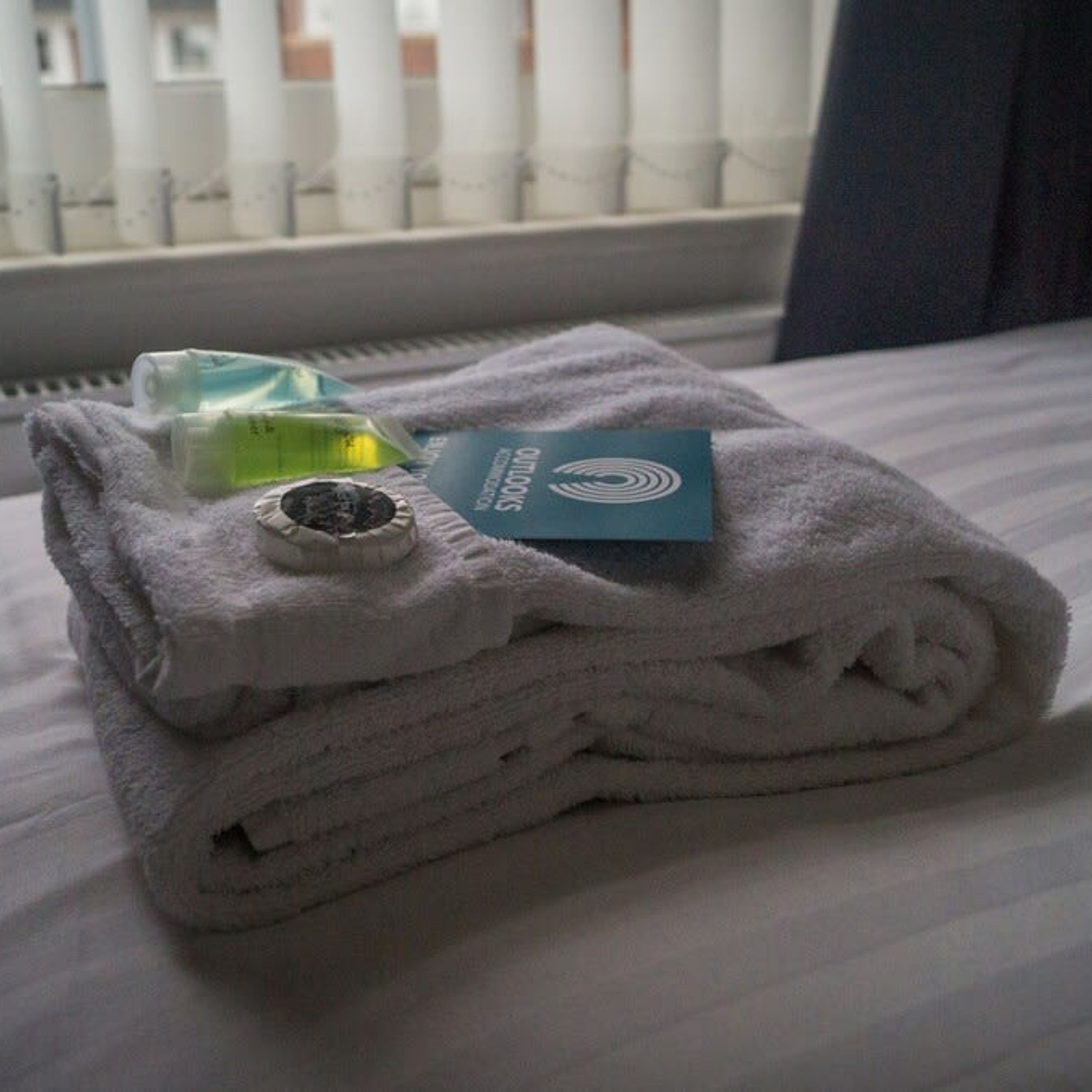 A neatly folded stack of towels on a bed with a window in the background.