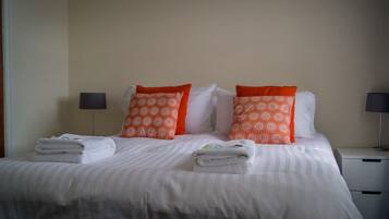A neatly made bed with white and orange patterned pillows, a striped blanket, and folded towels on the side.
