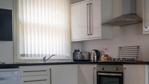A modern kitchen with white cabinetry, a built-in oven, a gas stove, and a window with blinds. - The Racecourse Gathering 5 Bed - Sleeps 12 City Centre (Chester)