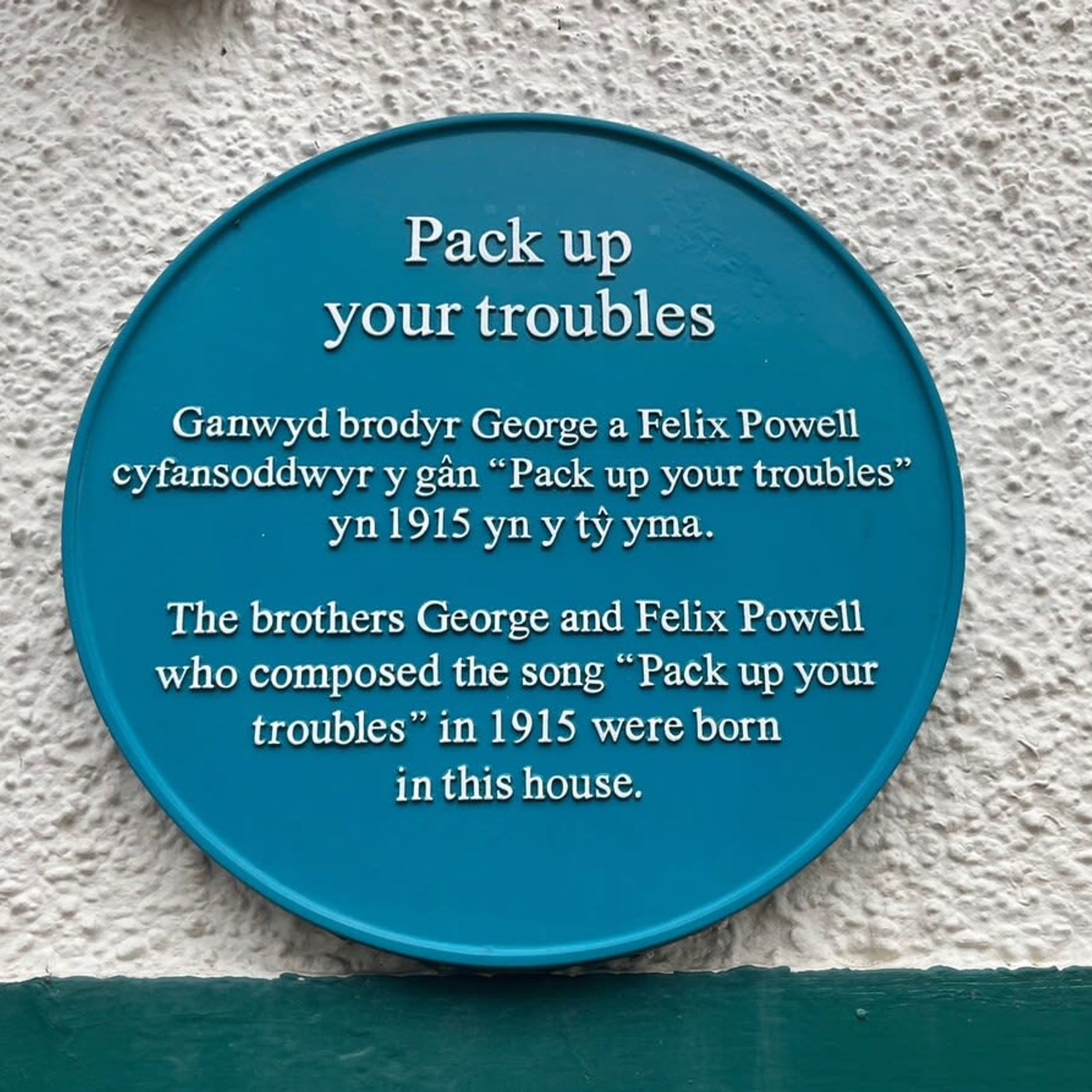 A blue plaque on a textured wall with text about the song "Pack up your troubles" by George and Felix Powell.