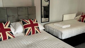 Une chambre d’hôtel avec deux lits, chacun doté d’une tête de lit, de draps blancs et d’oreillers ornés du motif Union Jack. Un miroir est accroché au mur, et il y a un radiateur blanc.