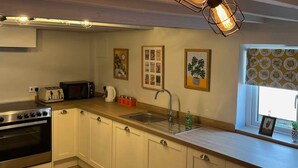 Une cuisine avec des meubles blancs, une cuisinière, un évier et une fenêtre agrémentée de rideaux à motifs.