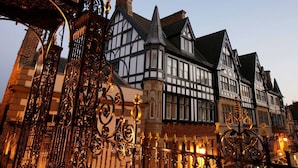 Un edificio histórico con arquitectura de estilo Tudor, que presenta una imponente torre de reloj y ornamentada rejería.