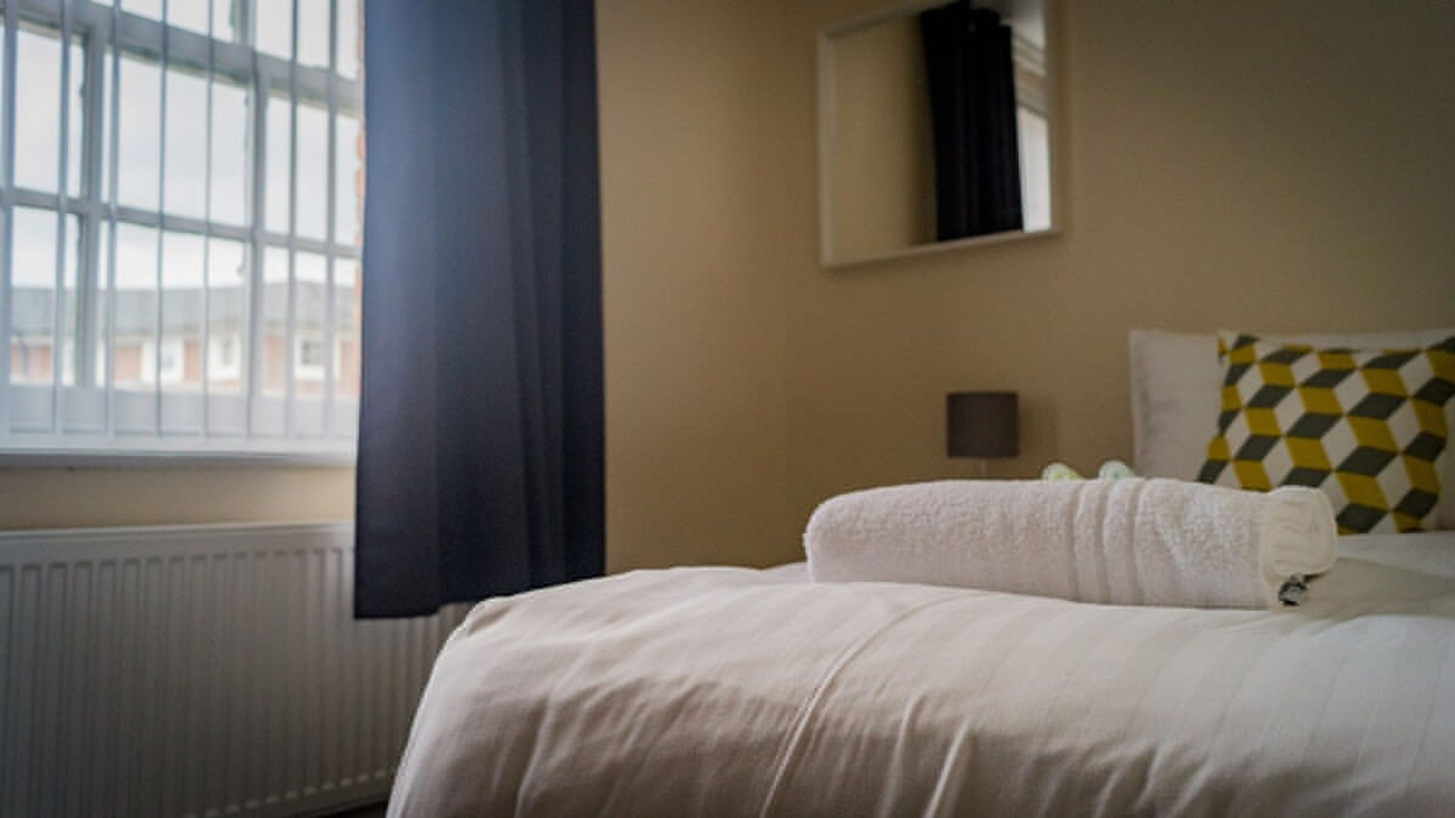 Une chambre d’hôtel avec un lit, une fenêtre avec des stores, un radiateur et un téléviseur fixé au mur.