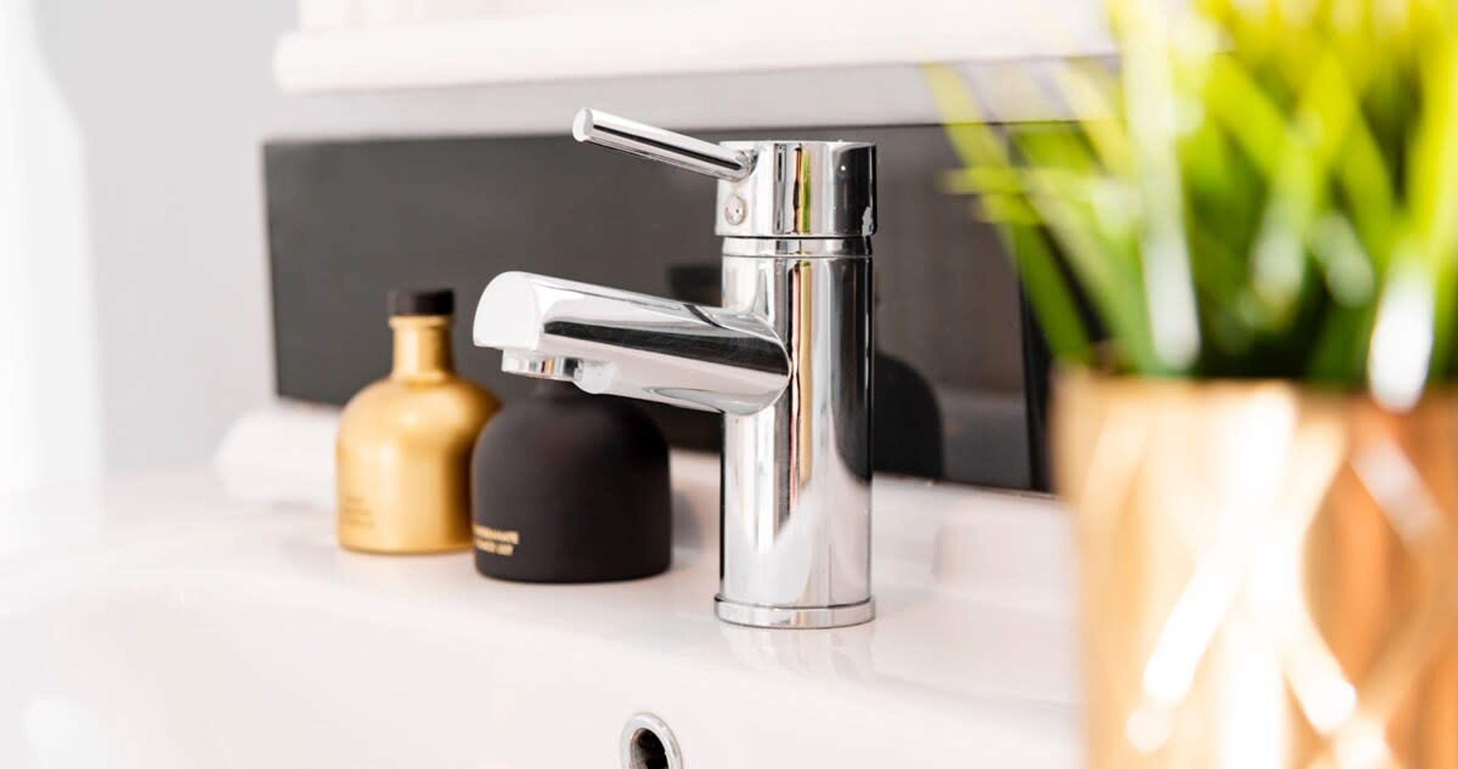 A modern chrome faucet on a white countertop with a black soap dispenser and a gold-colored container in the background.