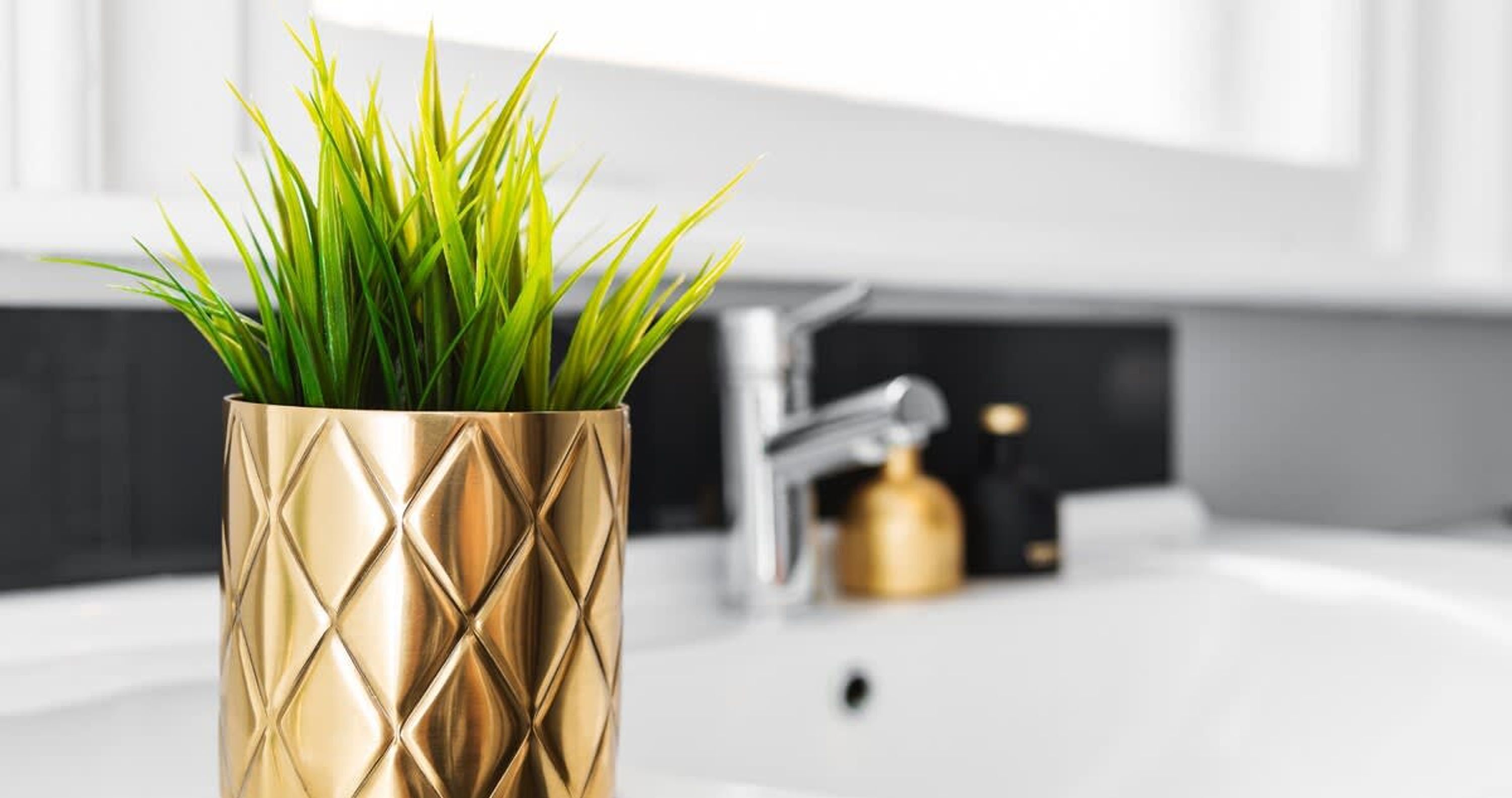 A gold vase with green grass on a modern kitchen counter.