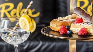 Eine Dessertplatte mit Gebäck und Beeren, ein Glas Wasser mit Trinkhalm und eine schwarze Couch mit gelbem Text im Hintergrund.