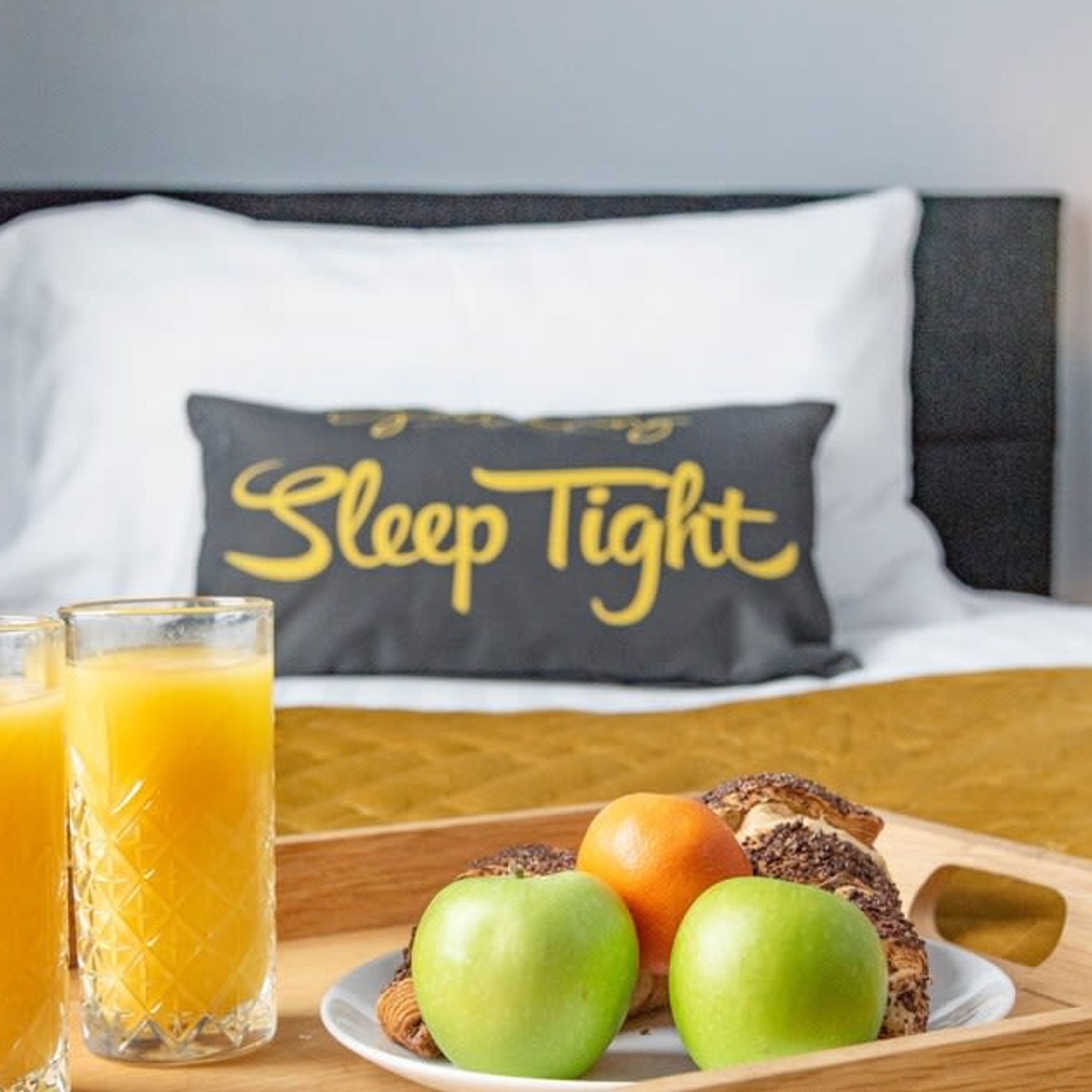 Ein Frühstücksbrett mit Äpfeln, einer Orange und einem Glas Orangensaft auf einem Holztisch in einem Hotelzimmer.