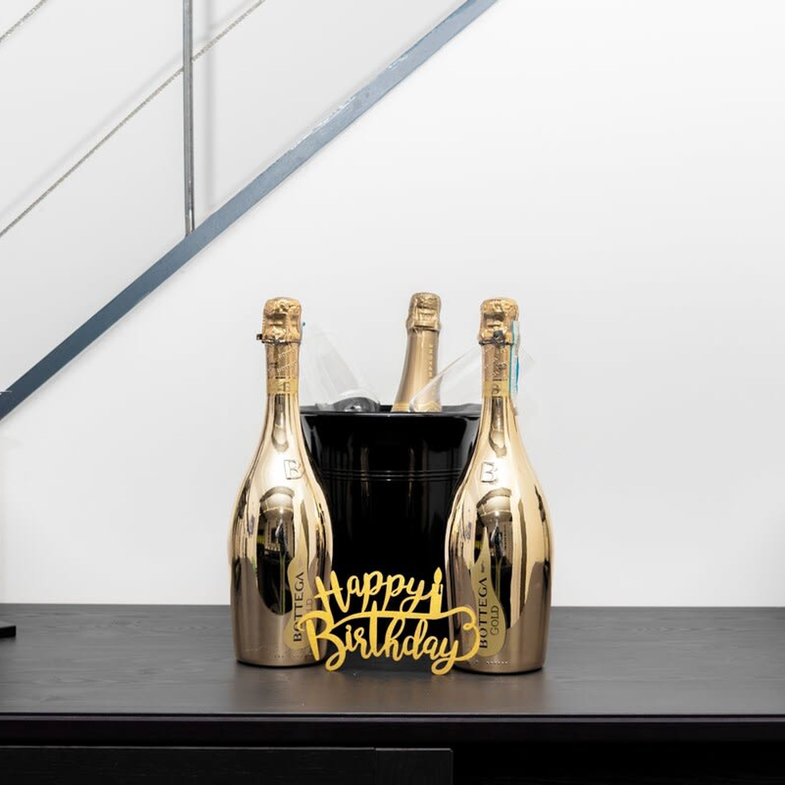 Three champagne bottles in a black holder with a "Happy Birthday" sign.
