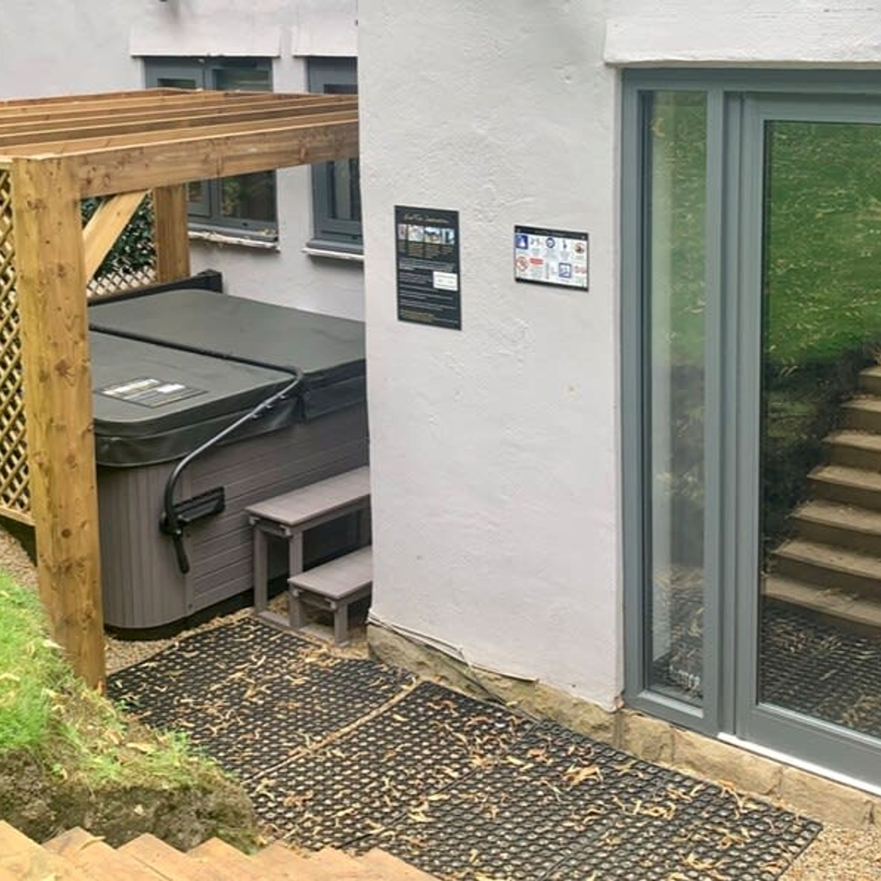 A hot tub with a wooden deck, a small set of steps, and a door leading to a covered outdoor area.
