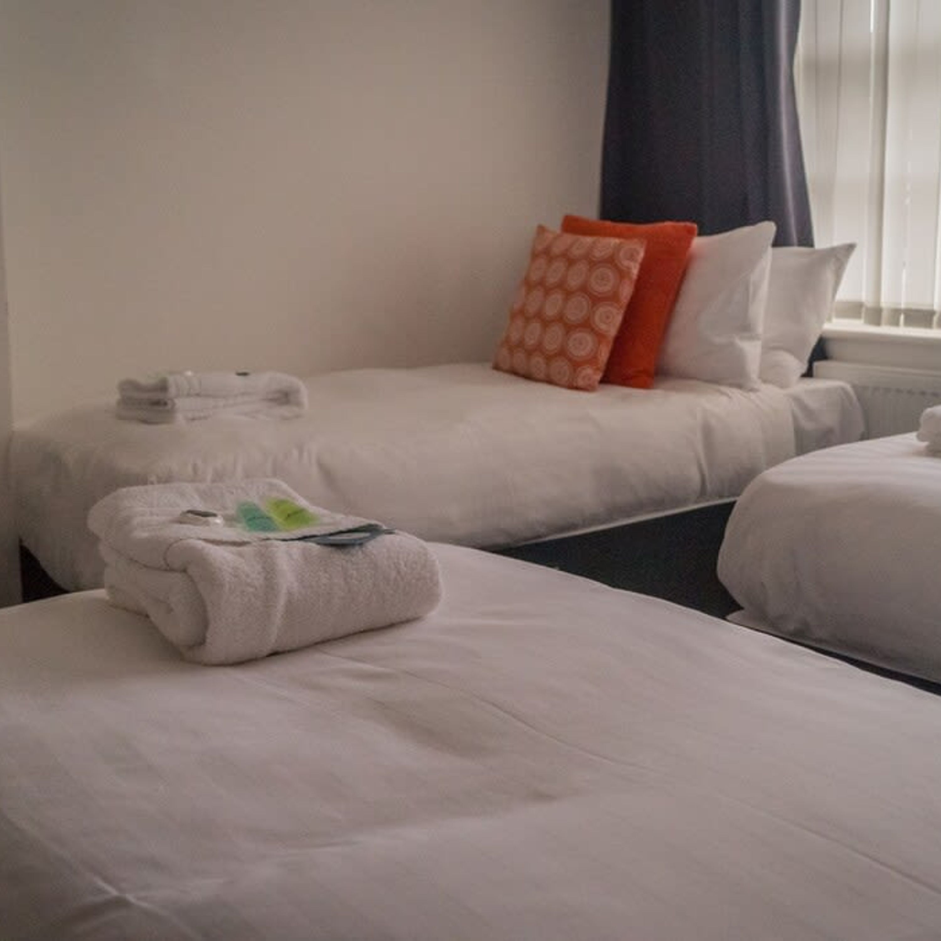 A hotel room with two beds, each with a white duvet and pillows, and a neatly folded towel on the bed.