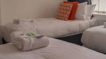 A hotel room with two beds, each with a white duvet and pillows, and a neatly folded towel on the bed.