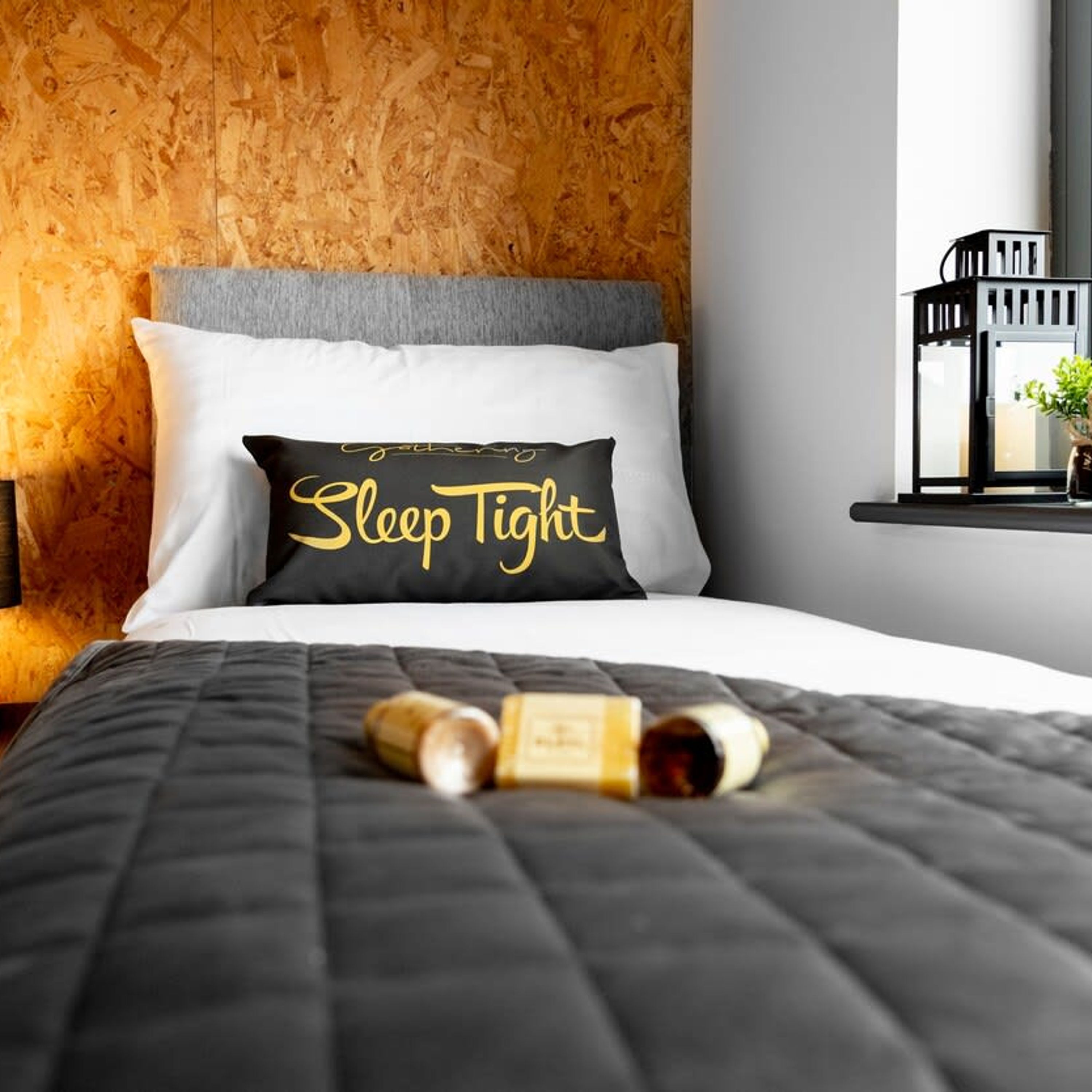 A neatly made bed with a black and white pillow that reads "Sleep Tight" and a bottle of wine on the bed.
