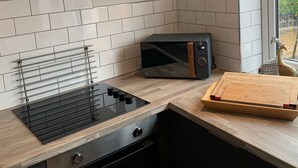 A modern kitchen with a black induction cooktop, a microwave, and a wooden cutting board. - The Bridgewater Studio The Gathering Sale (Sale)