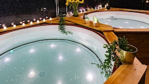A spa area with two hot tubs, surrounded by wooden benches and candles, under a canopy of greenery. - The Tudor Gathering Chester - City Centre (Chester)