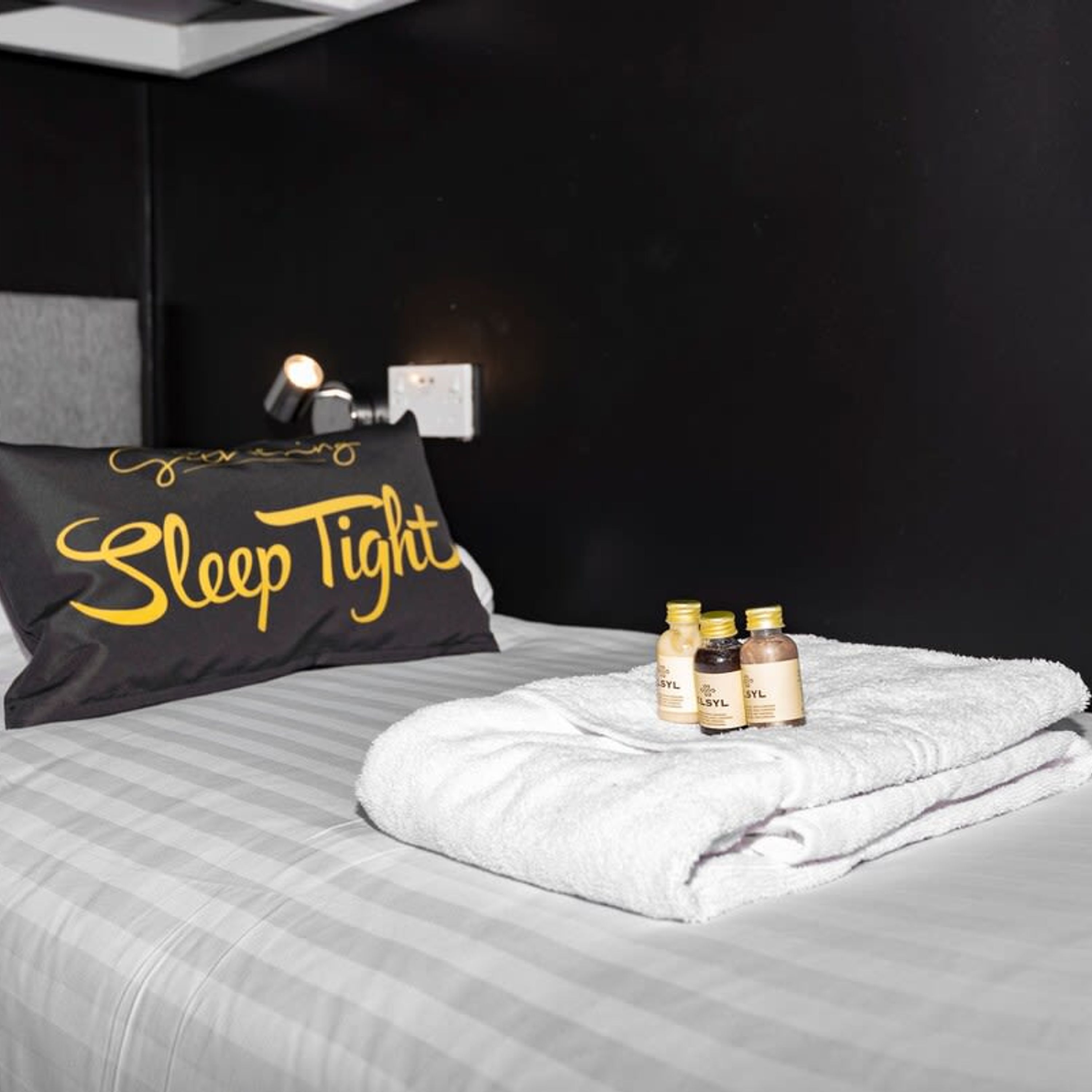 A neatly made bed with a pillow labeled "Sleep Tight" and three bottles of lotion on a white towel.