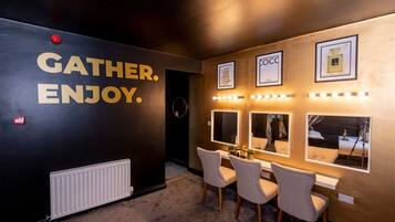 A hotel lobby with a black wall featuring the text "GATHER. ENJOY." and framed pictures of perfumes on the wall.