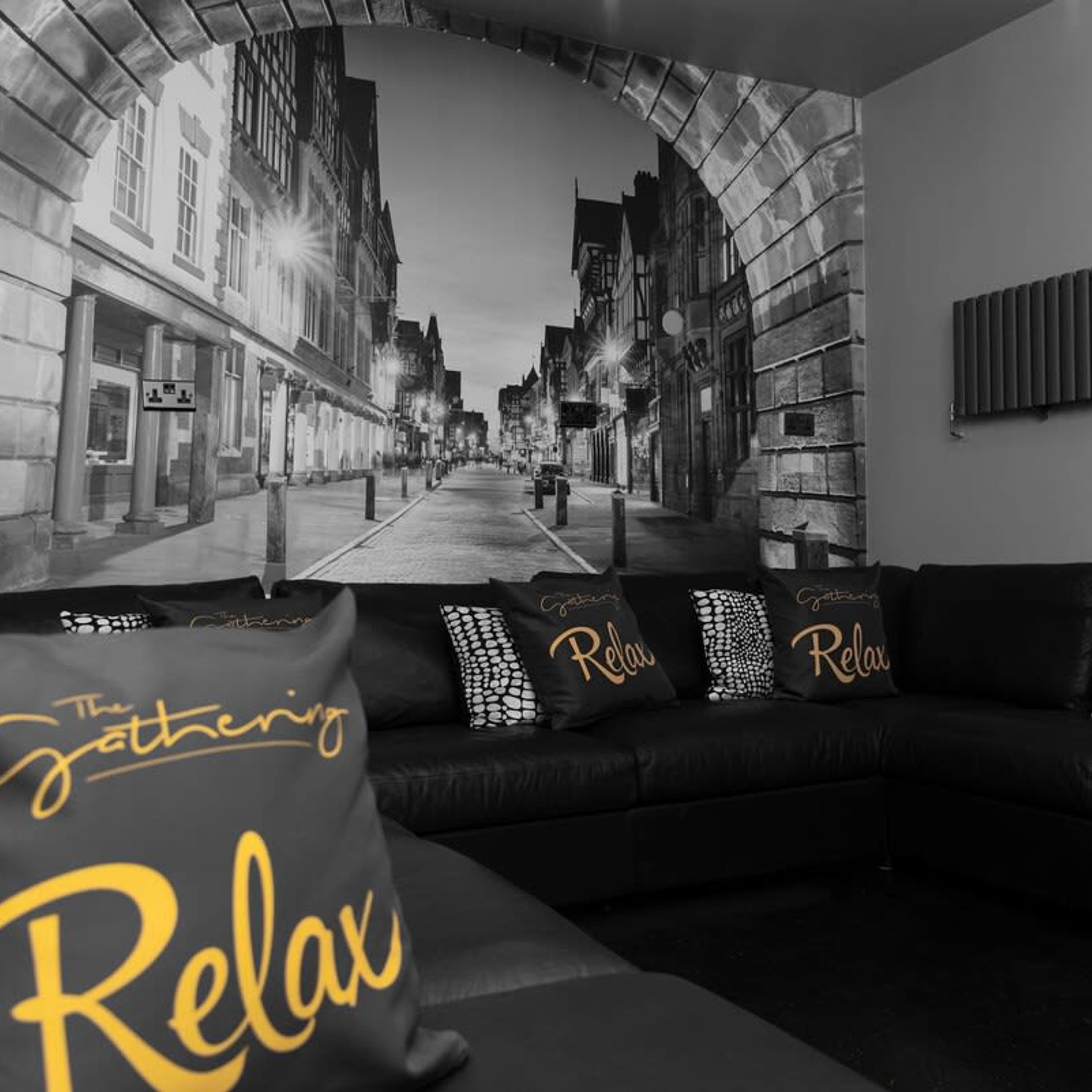 A black and white photograph of a street scene with buildings, a sofa with 'Relax' pillows, and a sign that reads 'The Gathering'.