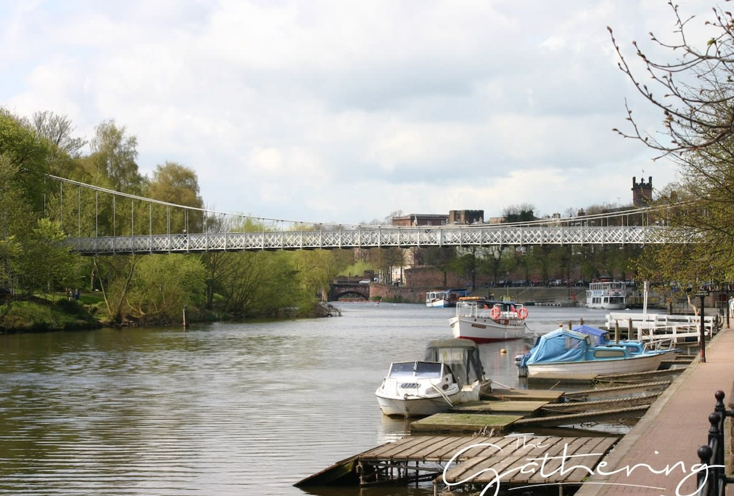 Un muelle a orillas del río con barcos, un puente y edificios al fondo.