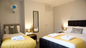 Une chambre d’hôtel avec deux lits, chacun recouvert d’une couvre-lit d’une couleur différente, une table de chevet avec une lampe, un miroir sur le mur et une porte.