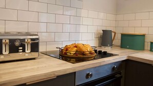 Une cuisine avec un dosseret de carrelage blanc, un grille-pain, un panier à pain, une bouilloire et un récipient vert posé sur le plan de travail.