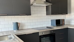 A modern kitchen with dark cabinets, a stainless steel range hood, a microwave, and a built-in oven. - The Castlefield The Gathering Sale (Sale)
