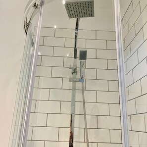 A shower with a glass door, white tiled walls, and a showerhead mounted on the wall. - The Castlefield The Gathering Sale (Sale)