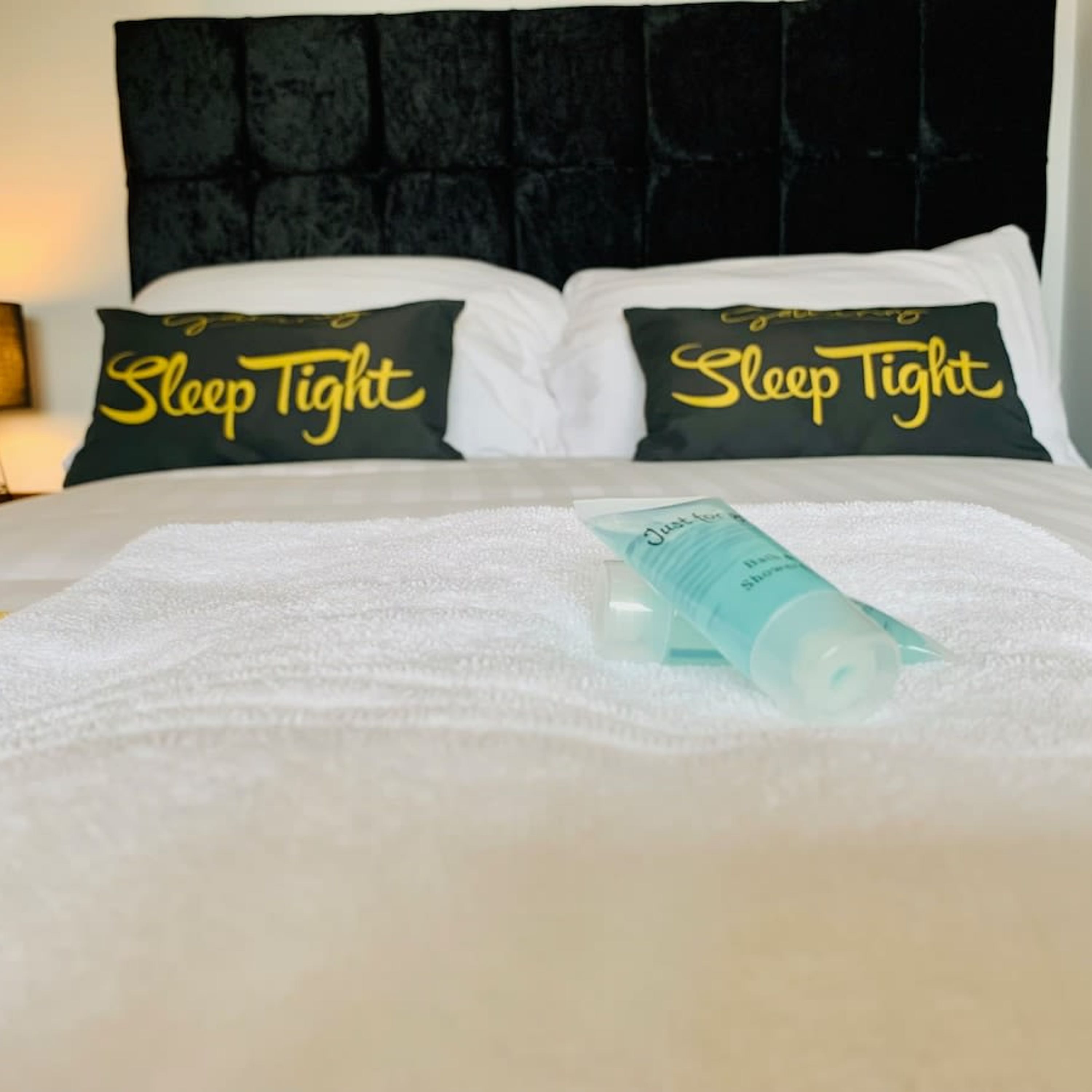 A neatly made bed with two pillows labeled "Sleep Tight" and a bottle of lotion on the bed.