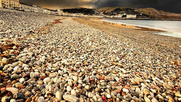 A pebbled beach with buildings in the background and a cloudy sky. - The North Wales Gathering - 9 Bedroom - EV Charging (Flint)