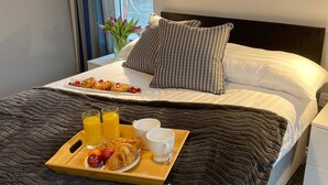 A neatly made bed with a dark quilt, a tray of breakfast including croissants, fruit, and orange juice, and a bedside table with a lamp. - The North Wales Gathering - 9 Bedroom - EV Charging (Flint)