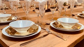 A dining table set with white bowls, gold cutlery, and champagne flutes, with a wooden table and a wall-mounted light fixture. - The North Wales Gathering - 9 Bedroom - EV Charging (Flint)