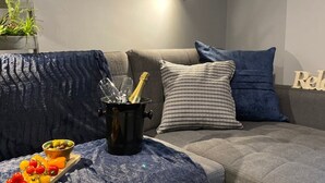 A cozy living room with a grey sofa, a blue throw blanket, and a small table with a bottle and glasses. - The North Wales Gathering - 9 Bedroom - EV Charging (Flint)