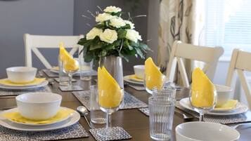 Una mesa de comedor dispuesta con cuencos blancos, servilletas amarillas y vasos transparentes, con un jarrón de flores blancas en el centro.