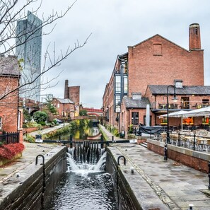 A canal with water flowing through it, flanked by brick buildings and a modern glass structure. - The Lower Gathering - Sale - Sleeps Up To 13 (Sale)