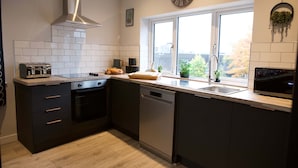 A modern kitchen with a built-in oven, dishwasher, and a large window with a view of trees. - The Gathering Sale - Sleeps Up To 22 (Sale)