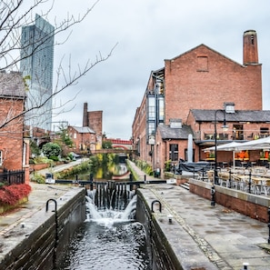 A canal with water flowing through it, flanked by brick buildings and a modern glass structure.