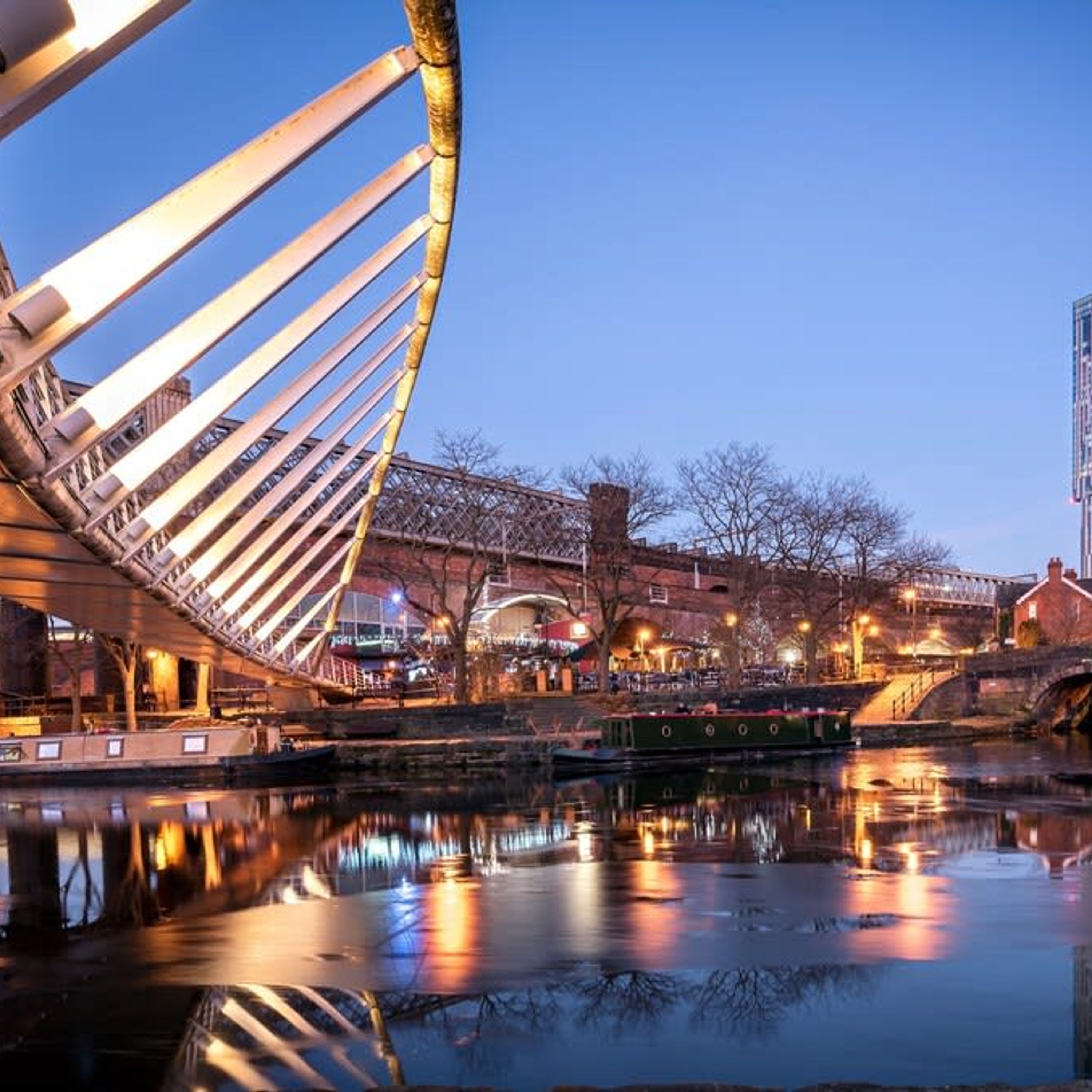 A modern bridge with a unique cable design, a river with a boat, and a cityscape with buildings and a bridge in the background.