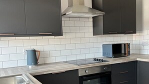 A modern kitchen with dark cabinets, a stainless steel range hood, a microwave, and a built-in oven. - The Islington Studio The Gathering Sale (Sale)