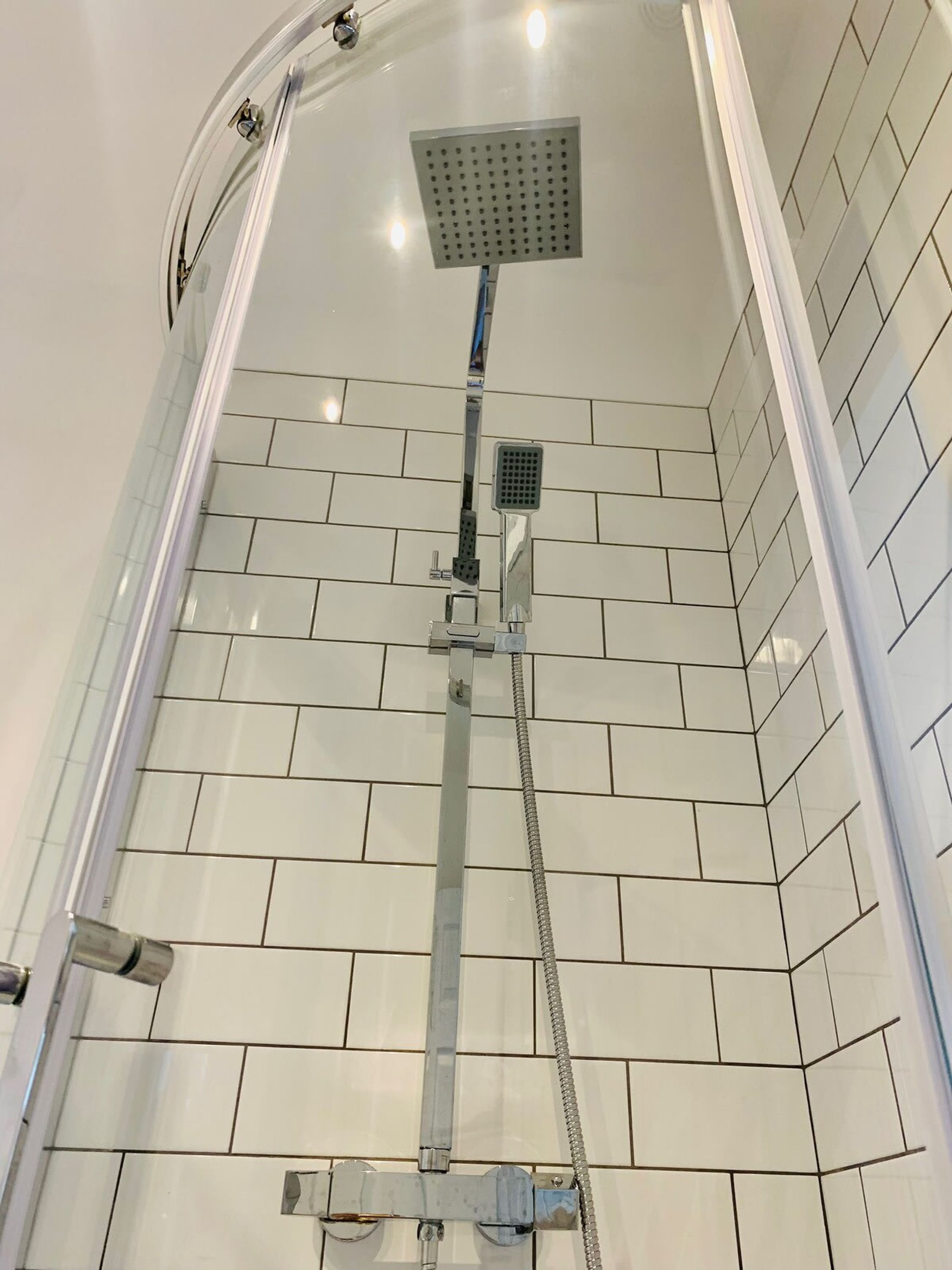 Eine Dusche mit einer eckigen Duschbrause, einer Handbrause und einem flexiblen Duschschlauch.