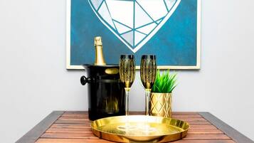 A framed abstract heart artwork on a wall, a black pot with a gold lid, two ornate glasses, a gold tray, and a potted plant on a wooden table.