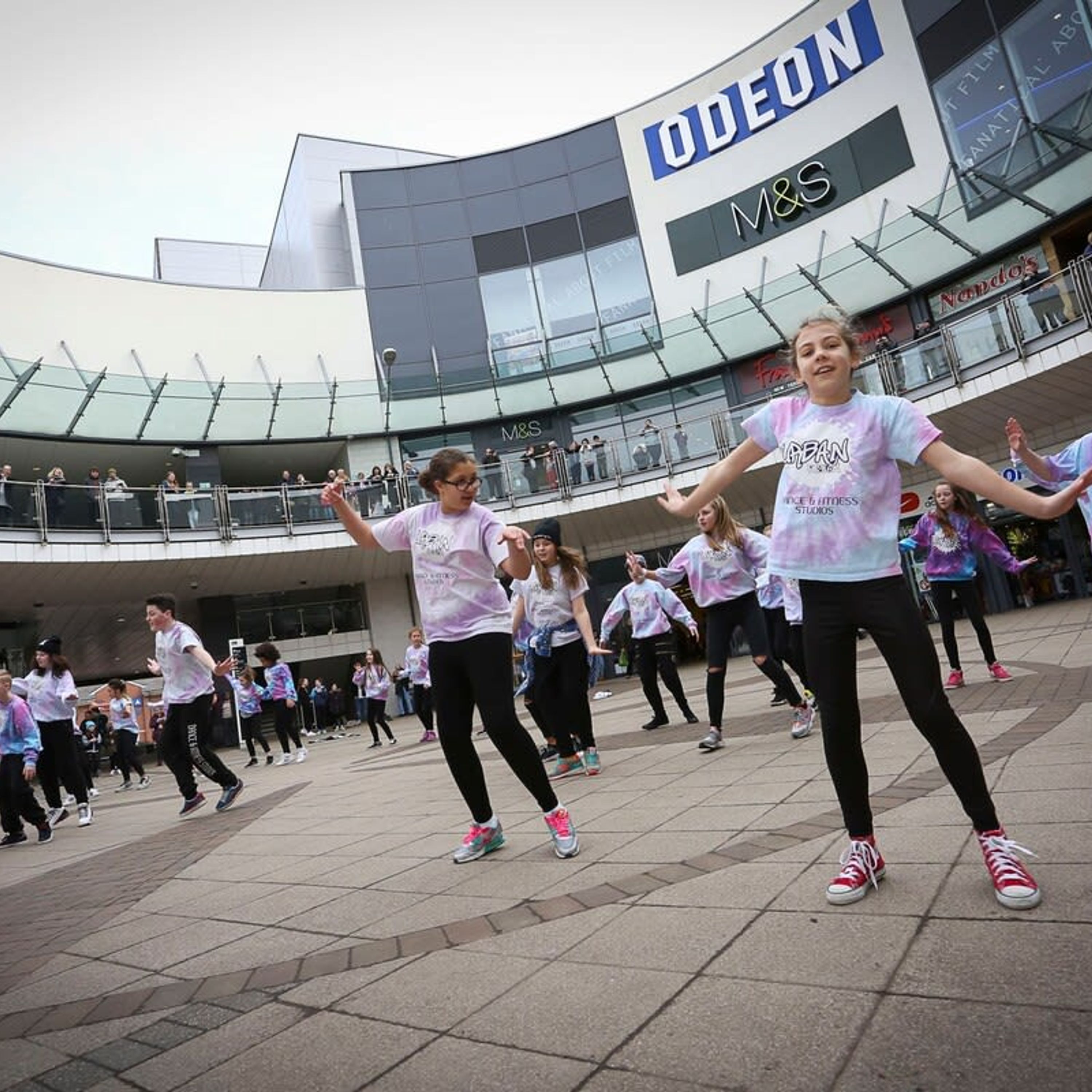 A group of people performing a dance routine in an outdoor area with a modern building in the background.