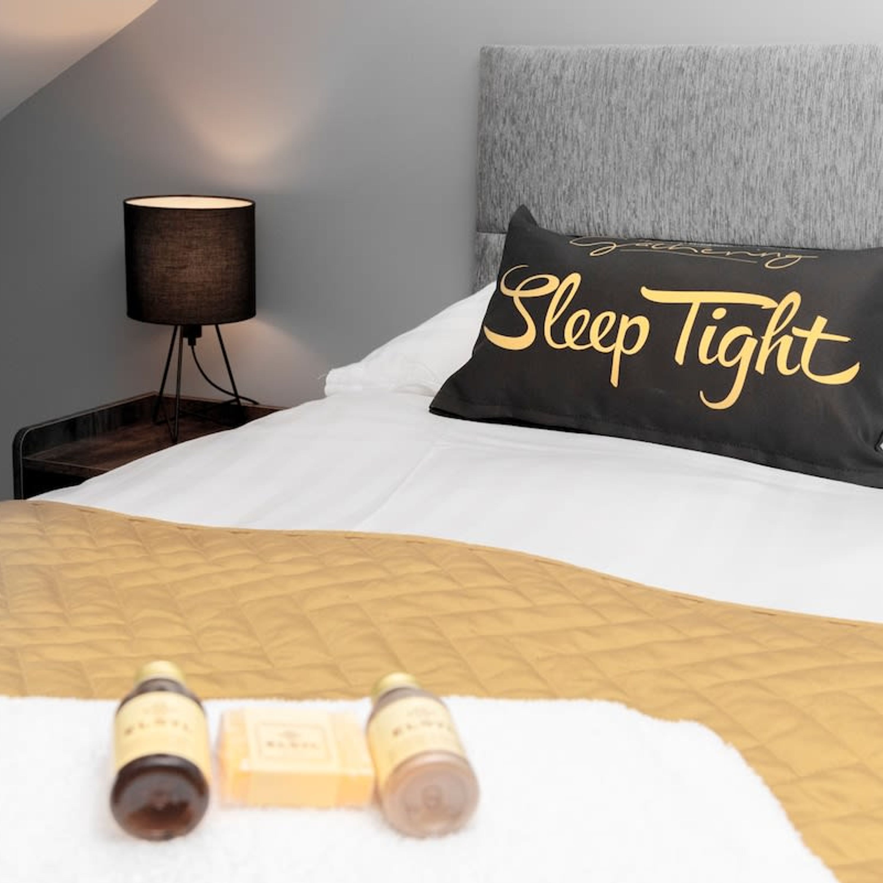 A neatly made bed with a pillow labeled "Sleep Tight" and two bottles on the bed.