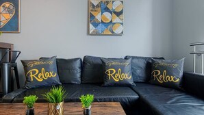 A modern living room with a black leather sofa, three 'Relax' pillows, two small potted plants, and a wooden coffee table. - The Eisteddfod - Berwyn House Central Wrexham (Wrexham)