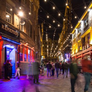 A bustling street at night with illuminated string lights and people walking.