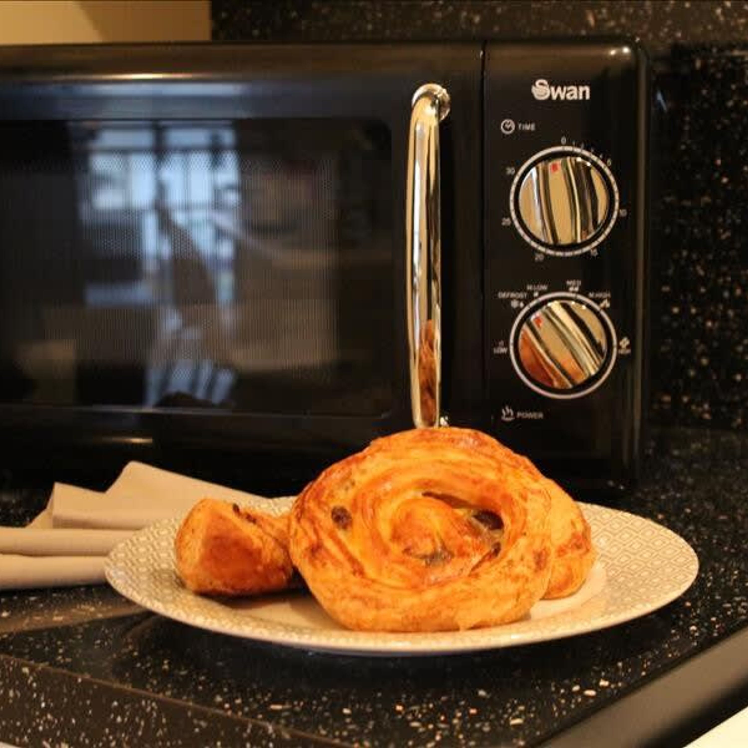 Un forno a microonde con un pannello di controllo, un piatto con un dolce e un tovagliolo su un piano di lavoro.