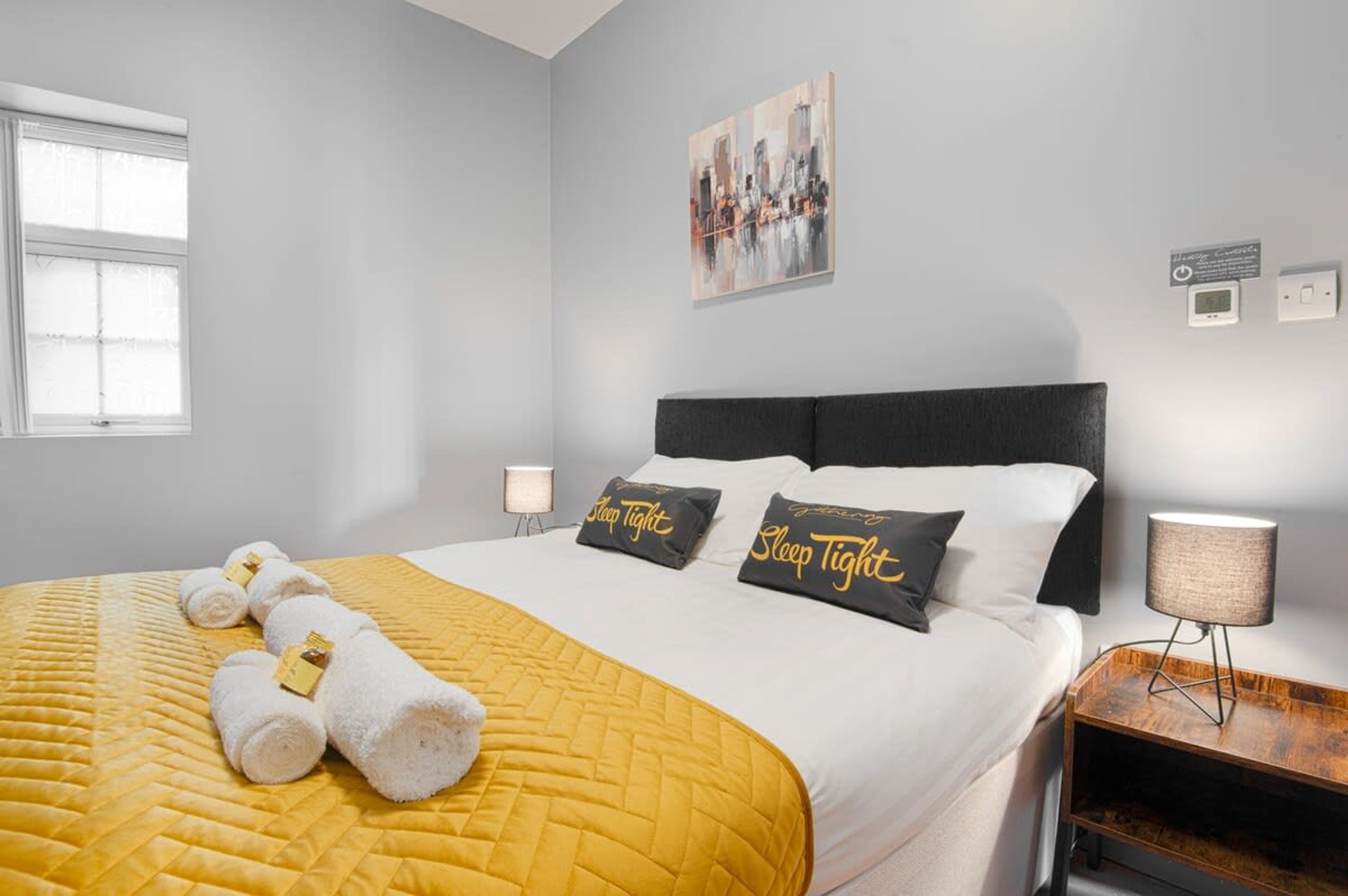 A hotel room with a bed, a bedside lamp, a nightstand, and a painting on the wall.